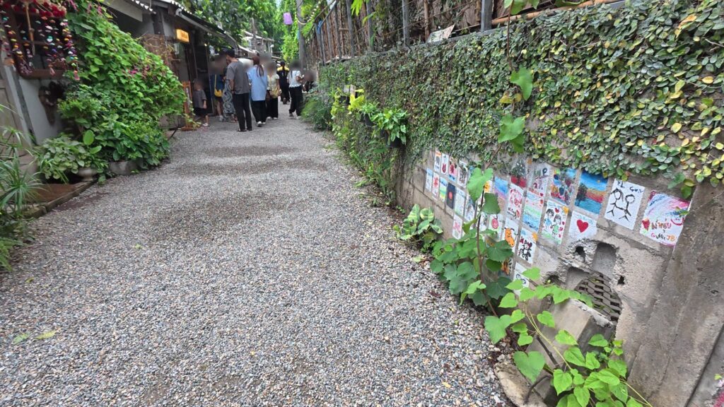 タイルアート作品が並ぶ壁沿いの小道を歩く観光客