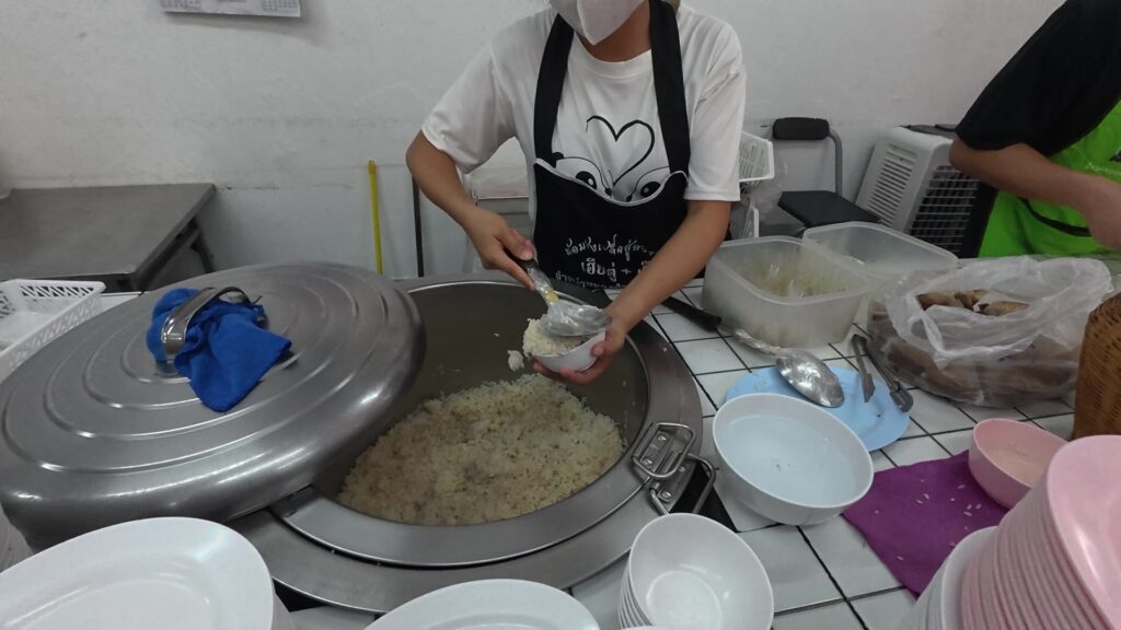 大きな寸胴鍋からご飯をよそうスタッフ